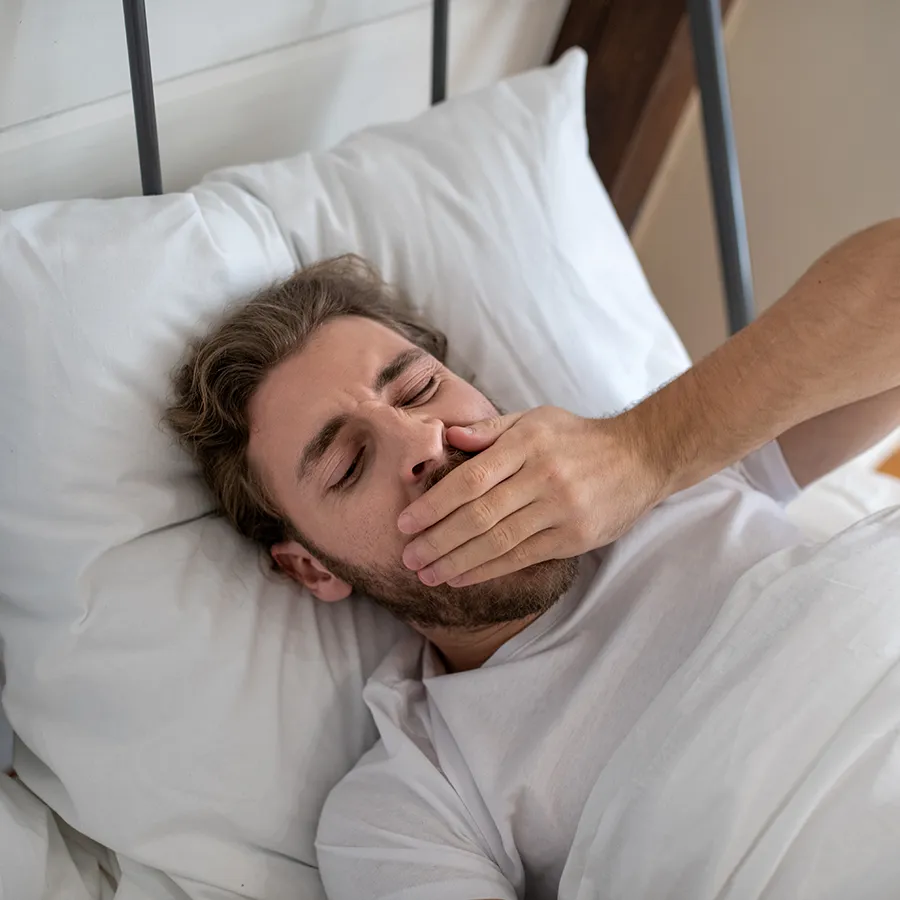 Man Lying in Bed with Hand Over Mouth